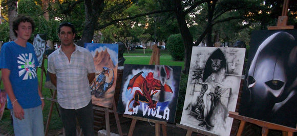 Maximiliano Cabaleiro y un alumno suyo, junto a los cuadros que expusieron en la plaza San Martín. 