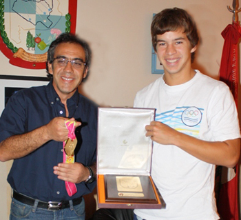 Andreasen muestra la placa y Guzmán sostiene la medalla de oro del joven.